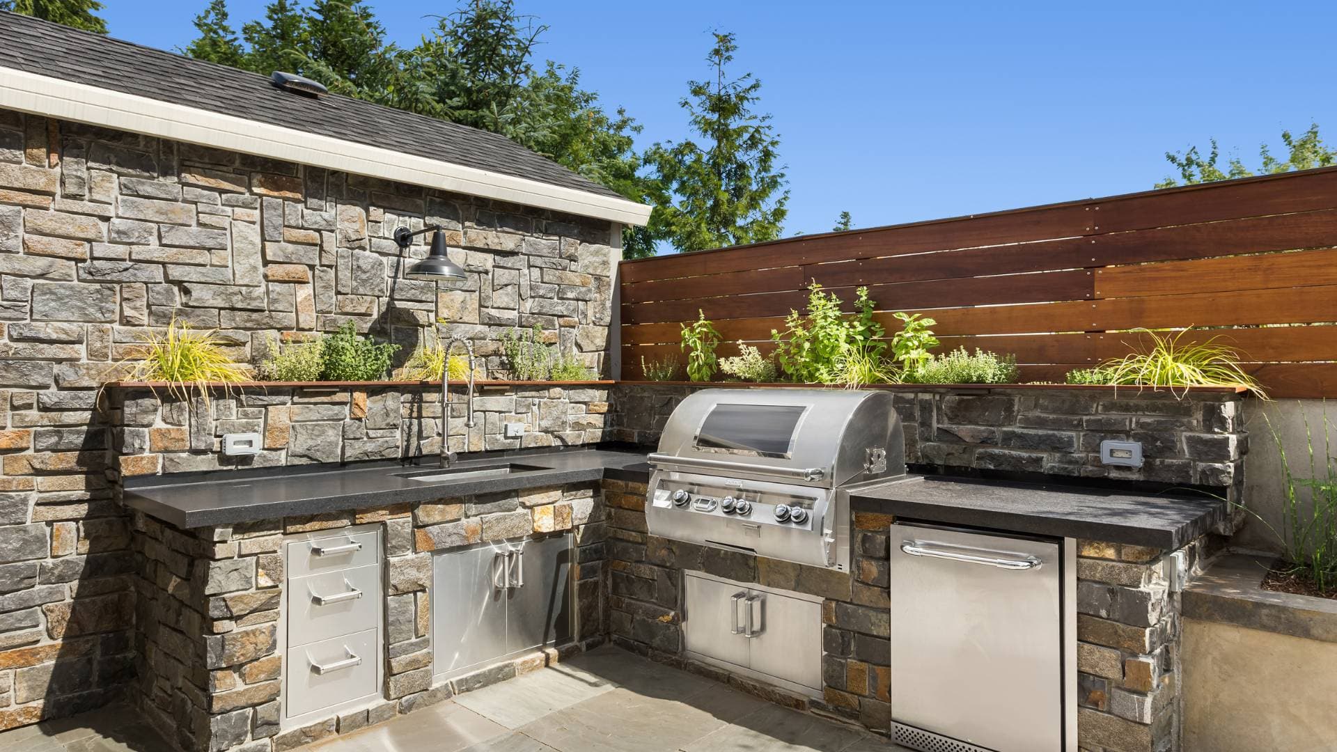 Stone-faced outdoor kitchen and seating built against a rear elevation